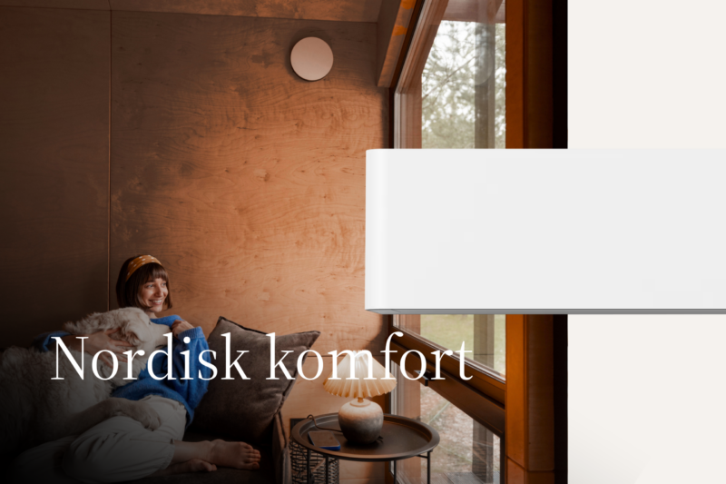 Vit luftvärmepump i ett varmt, träklätt vardagsrum; en person vilar avslappnat på soffan vid fönstret — lugn, nordisk komfort.